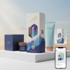 A display of Aurora Glow skincare products on white platforms, including a blue cream jar, a serum bottle in a box, and a light blue tube, with soft sky background. A smartphone at bottom right shows the same product image on social media.
