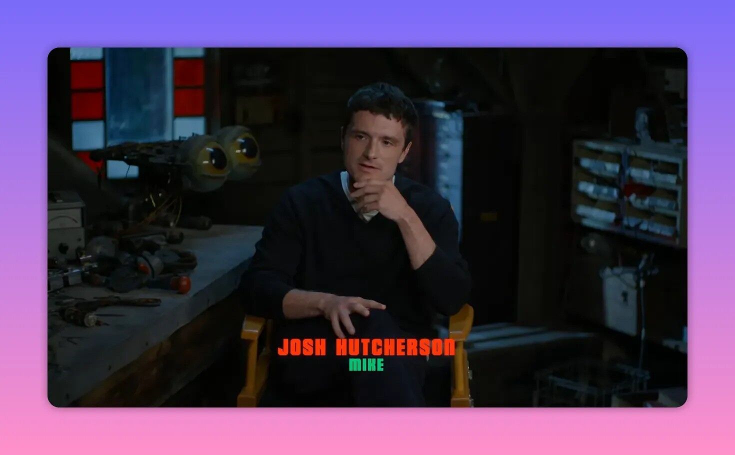 Male actor seated in a workshop-style interview chair with animatronic parts on a workbench behind him