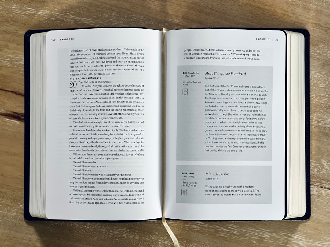 An open book lies on a wooden surface, showing two pages. The left page contains text with the heading "The Ten Commandments" and the number 20. The right page has regular text and two shaded text boxes featuring quotes and commentary.